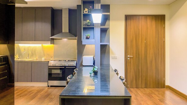 A modern kitchen with a central island, built-in appliances, and a wooden door. - Spacious and Cozy 2BR Apartment Kemang Village (Jakarta)