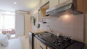 A modern kitchen with a gas stove, sink, and stainless steel range hood. There is a bed with white bedding in the adjacent room. - Good Deal and Comfy Studio Apartment at Cinere Bellevue Suites (Depok)