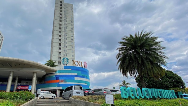 A tall building with a curved structure in front, a palm tree, and a sign with 'XXI' on top. - Good Deal and Comfy Studio Apartment at Cinere Bellevue Suites (Depok)