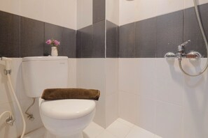 Un baño con inodoro, ducha y un florero con flores en la pared.