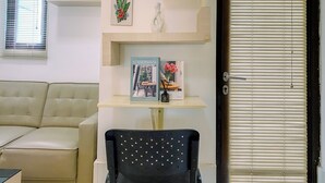 Ein Wohnzimmer mit einem beigen Sofa, einem schwarzen Sessel, einem Holzregal mit Dekoration und einem Fenster mit Jalousien.