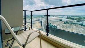 Ein Balkon mit Metallgeländer, einem Stuhl und Blick auf ein Industriegebiet mit Gebäuden und Grünflächen.