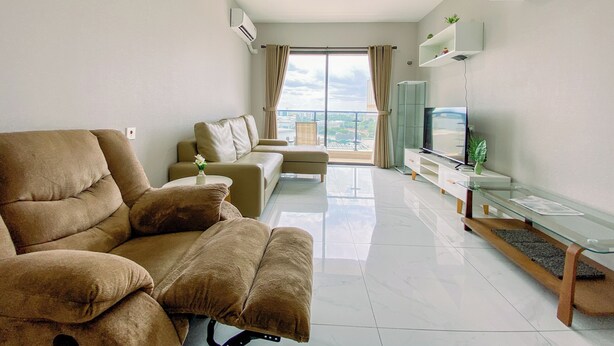 Ein modernes Wohnzimmer mit einer Couch, einem Fernsehtisch und einem Balkon mit Blick auf die Stadt.