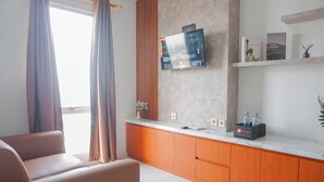 Een moderne hotelkamer met een bank, een flatscreen televisie aan de muur, een houten kast en een klein plankje met boeken en een waterfles.
