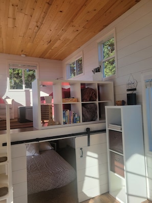 Cozy room with a high ceiling, wooden beams, and a welcoming atmosphere, featuring a bunk bed, desk, and bookshelf.