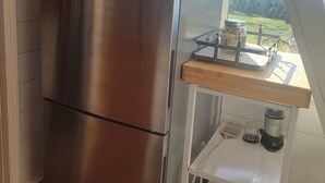 A stainless steel refrigerator in a kitchen with a wooden countertop and a view of a green landscape through a window.