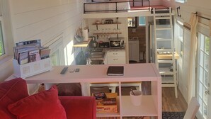 A cozy interior with a red sofa, a white coffee table, a loft bedroom with a bed, and a kitchen area with a microwave and sink.