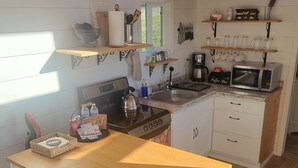 A compact kitchen with a wooden countertop, a kettle, a coffee maker, and a microwave. There are two chairs and a small dining table.