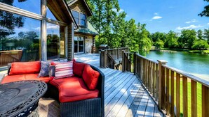A log cabin with a deck overlooking a river, featuring a wicker sofa and a table. - Lakefront Lake Anna Log Cabin, Views, Dock, Deck (Bumpass)