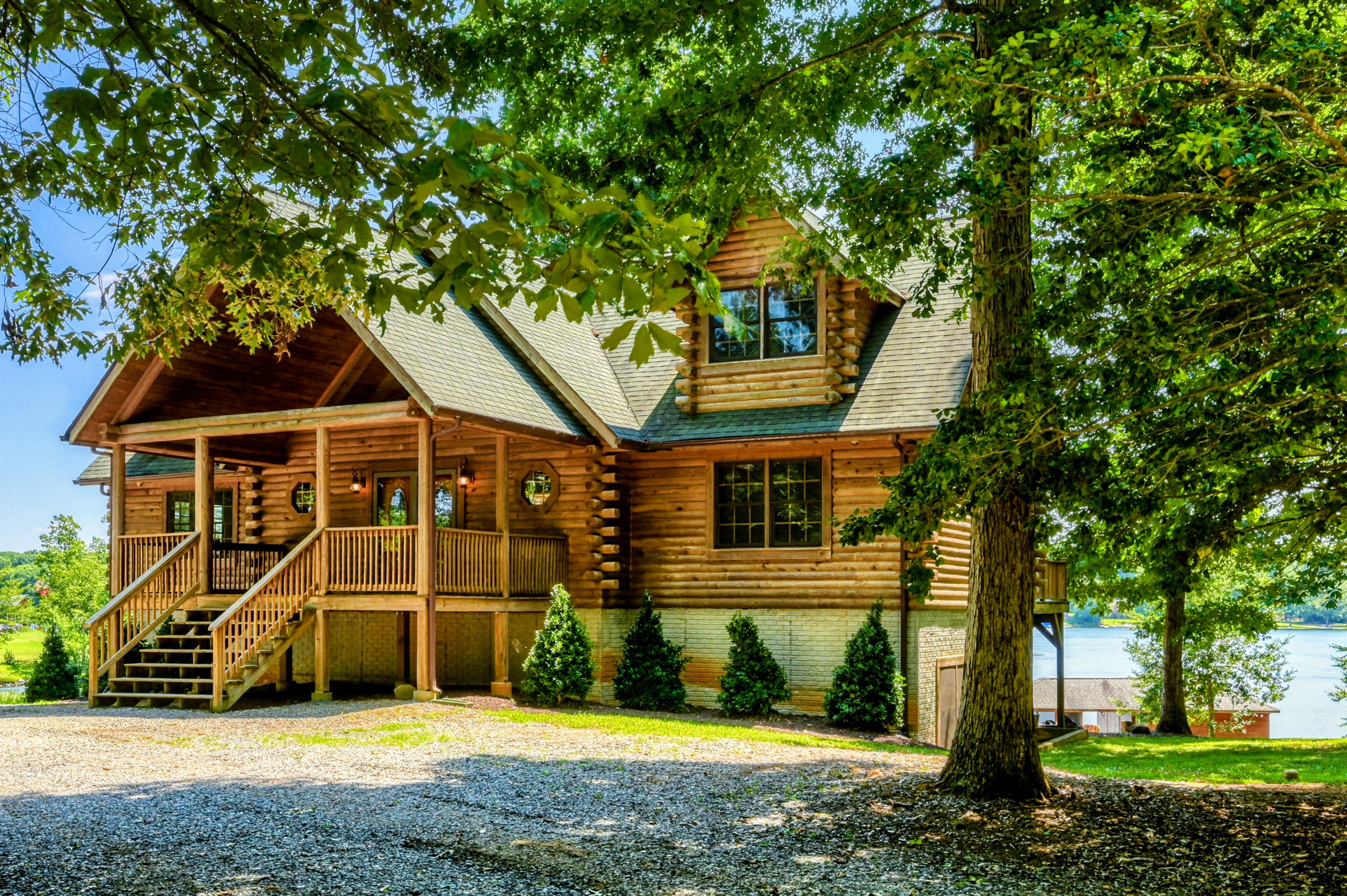 A log cabin with a porch, a staircase, and a view of a body of water.