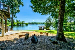 A lakeside view with a wooden deck, a fire pit, and a cabin. - Lakefront Lake Anna Log Cabin, Views, Dock, Deck (Bumpass)