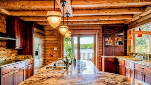 A kitchen with wooden walls, granite countertops, and pendant lighting. - Lakefront Lake Anna Log Cabin, Views, Dock, Deck (Bumpass)