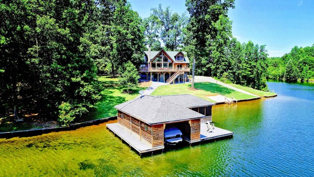 A lakeside cabin with a dock, surrounded by dense trees. - Lakefront Lake Anna Log Cabin, Views, Dock, Deck (Bumpass)