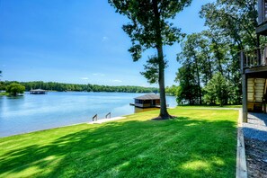 A lakeside property with a dock, a small building, and a well-maintained lawn. - Lakefront Lake Anna Log Cabin, Views, Dock, Deck (Bumpass)