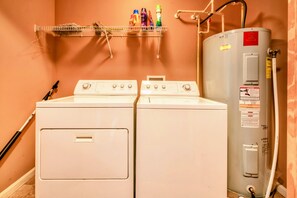 A laundry area with two front-loading washing machines, a water heater, and a shelf with various bottles. - Lakefront Lake Anna Log Cabin, Views, Dock, Deck (Bumpass)