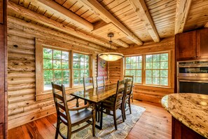 A wooden cabin interior with a dining table, chairs, a chandelier, and large windows. - Lakefront Lake Anna Log Cabin, Views, Dock, Deck (Bumpass)