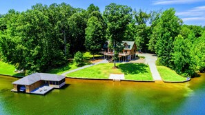 A lakeside property with a main house, a dock, and a well-maintained lawn. - Lakefront Lake Anna Log Cabin, Views, Dock, Deck (Bumpass)