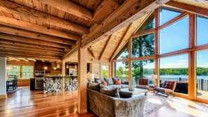 A spacious living area with a large couch, wooden flooring, and a view of a lake through large windows. - Lakefront Lake Anna Log Cabin, Views, Dock, Deck (Bumpass)