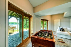 A bright and inviting game room features a foosball table and large glass doors with lake views. - Lakefront Lake Anna Log Cabin, Views, Dock, Deck (Bumpass)
