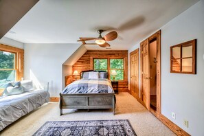 A bedroom with a bed, a nightstand, a lamp, a ceiling fan, and a view of the outdoors through a window.