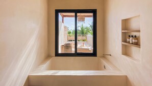 A bathroom with a bathtub, a window, and a shelf with toiletries. - Chic Beach suite with Plunge Pool in Tulum Hotel Zone (Tulum)