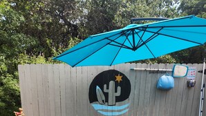 A round above-ground pool with a blue umbrella, a cactus logo, and a 'Redneck Cowboy Pool' sign on a wooden fence.