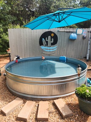 A round above-ground pool with a blue umbrella, a cactus logo, and a 'Redneck Cowboy Pool' sign on a wooden fence.