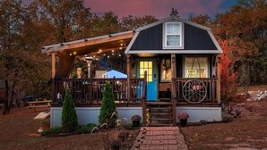A rustic cabin with a porch, a wheelbarrow, and string lights.