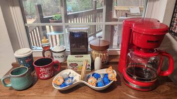 A kitchen counter with a coffee maker, sugar container, tea sampler, and various mugs.