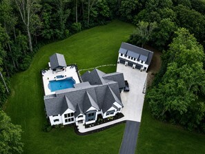 A large house with a swimming pool, surrounded by a well-maintained lawn and dense trees.
