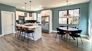 A modern kitchen with a central island, stainless steel appliances, and a dining area with a round table and chairs. - Luxury Guest House w/Resort Style Pool & Spa, pets welcome (Huntersville)