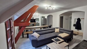 Un salon moderne avec un canapé d’angle gris, une table à manger en bois et un escalier rouge.