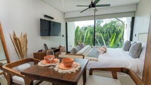 Quarto moderno com uma cama grande, TV na parede e varanda com vista para o verde.