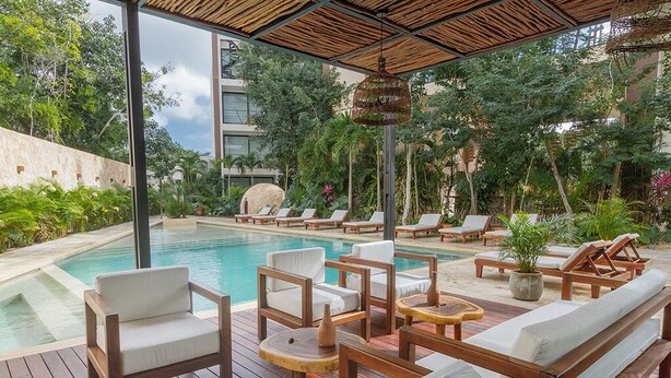 Área da piscina com espreguiçadeiras de madeira, cadeiras de descanso e uma pequena mesa.
