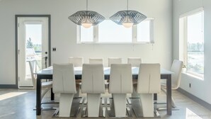 Un comedor moderno con una mesa larga y seis sillas, ventanas amplias y lámparas colgantes.