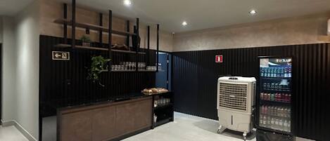A modern reception area with a dark reception desk, a wall-mounted plant, and a beverage dispenser.