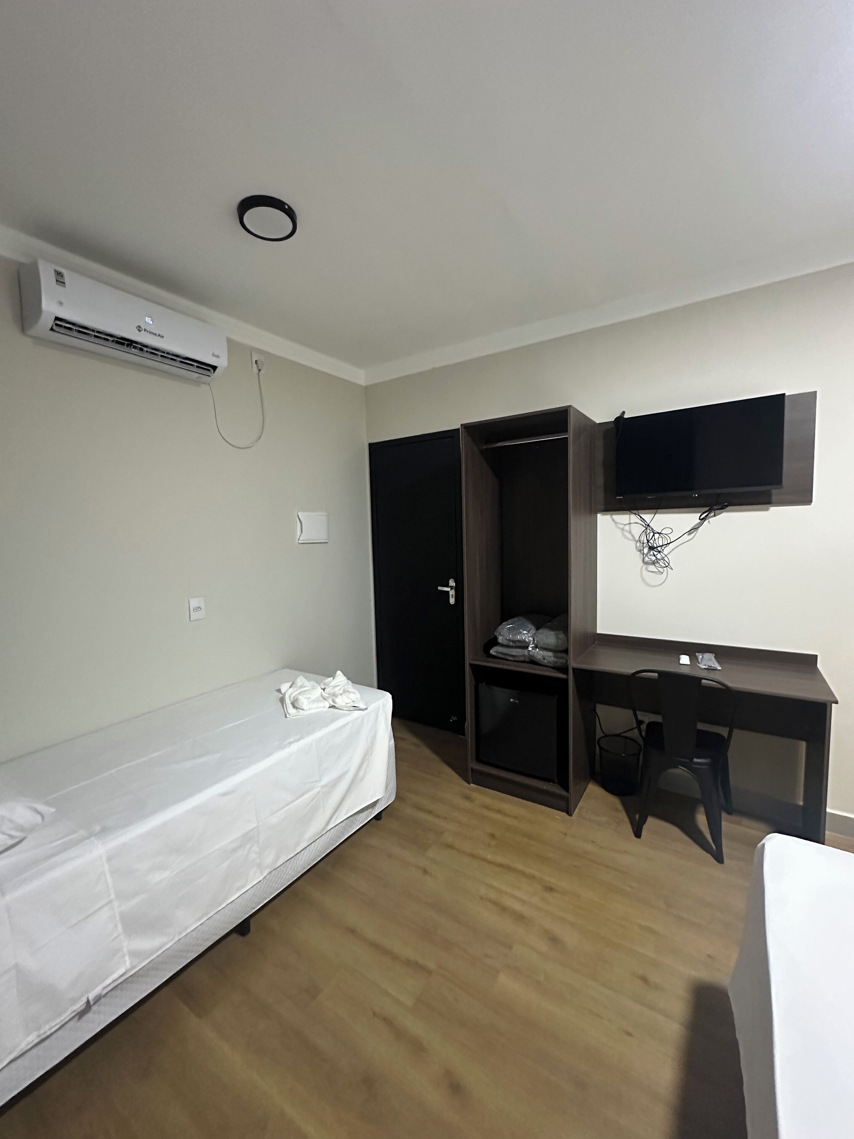 Una habitación pequeña y con pocos muebles, con una cama, un escritorio, un televisor montado en la pared y un aire acondicionado.