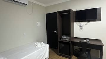Habitació petita i poc moblada amb un llit, un escriptori, un televisor fixat a la paret i un aparell d'aire condicionat.