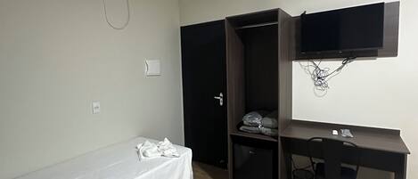 Una habitación pequeña y con pocos muebles, con una cama, un escritorio, un televisor montado en la pared y un aire acondicionado.