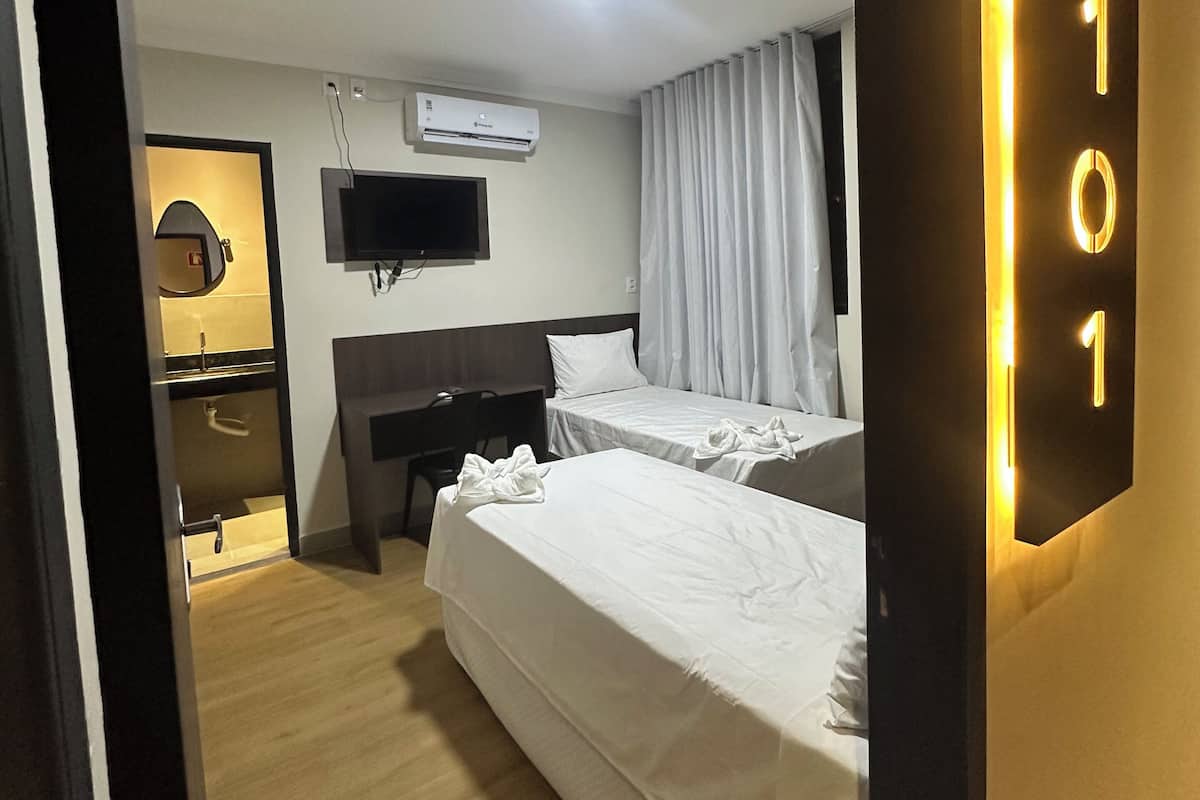 Ein Hotelzimmer mit zwei Betten, einem Schreibtisch, einem Fernseher und einer Klimaanlage.