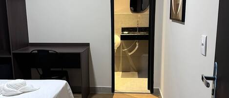Habitación de hotel con cama, escritorio, armario y baño visible a través de una puerta abierta.