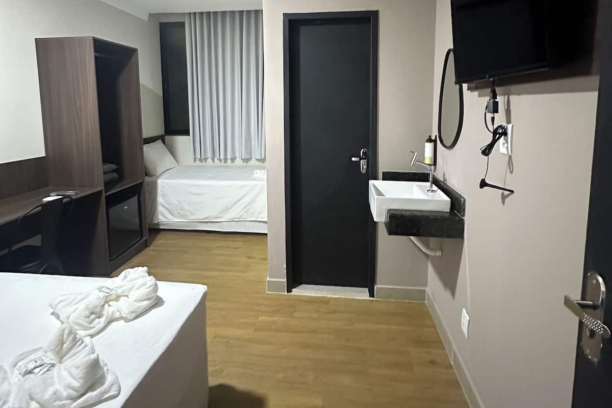 Ein Hotelzimmer mit Bett, Schreibtisch, Kleiderschrank und einem Badezimmer mit Waschbecken und Spiegel, sowie einer Klimaanlage.