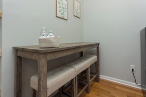 A wooden table with a woven basket containing bottles, a bench, and framed botanical prints on the wall. - Conductor's Suite at the Depot in charming Shenandoah (Shenandoah)