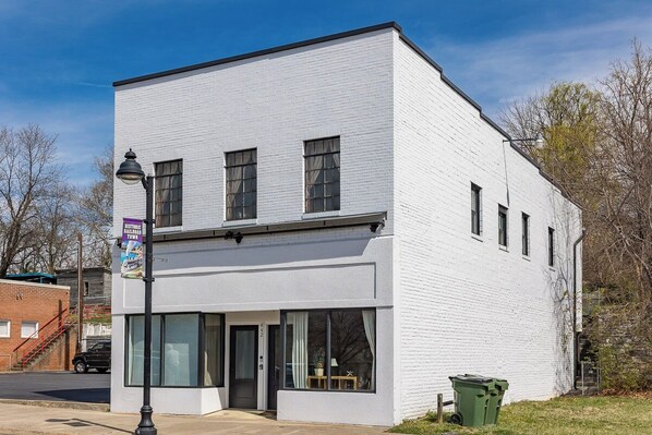 A white building with large windows and a door, a trash bin, and a street lamp. - Conductor's Suite at the Depot in charming Shenandoah (Shenandoah)