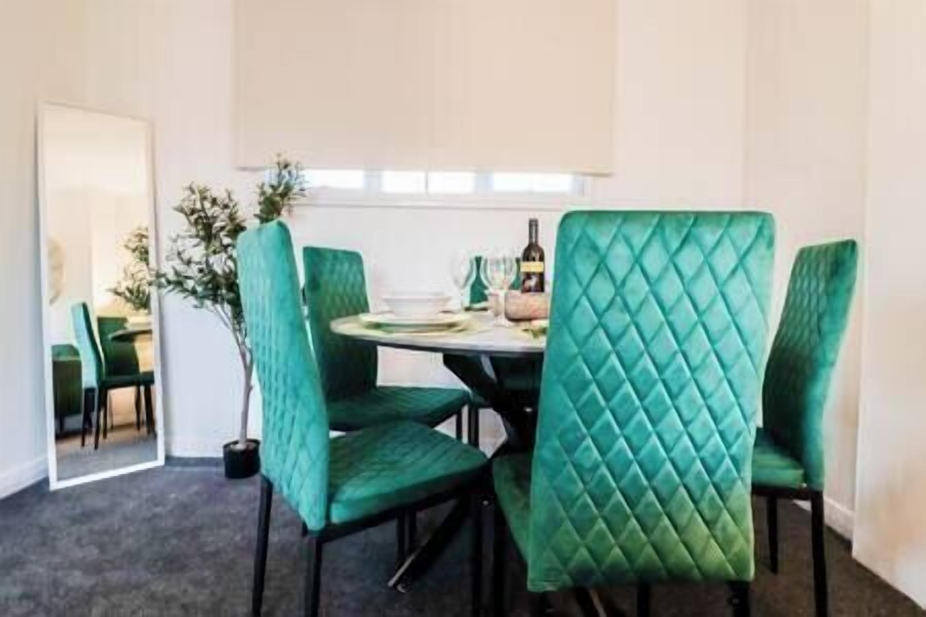A dining area with teal upholstered chairs and a round table.