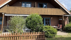 Een herenhuis met twee verdiepingen, een houten gevel, een pannendak en een omheinde tuin met beplanting.