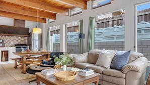 A cozy living room with a wooden ceiling, a beige sofa, a coffee table, and a dining area with a wooden table and chairs. - California Dreamin by Avantstay Private Pool + Fire Pit Near the Beach (Carlsbad)