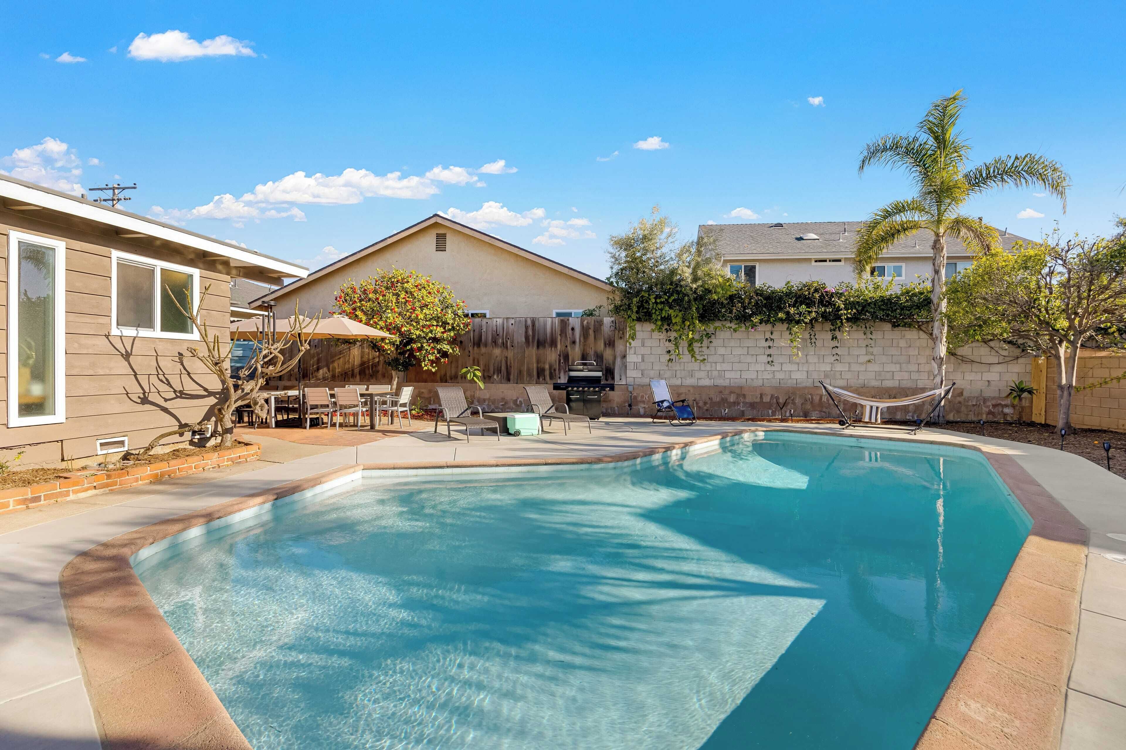 A backyard with a swimming pool, a hammock, and a patio area with chairs and a table.