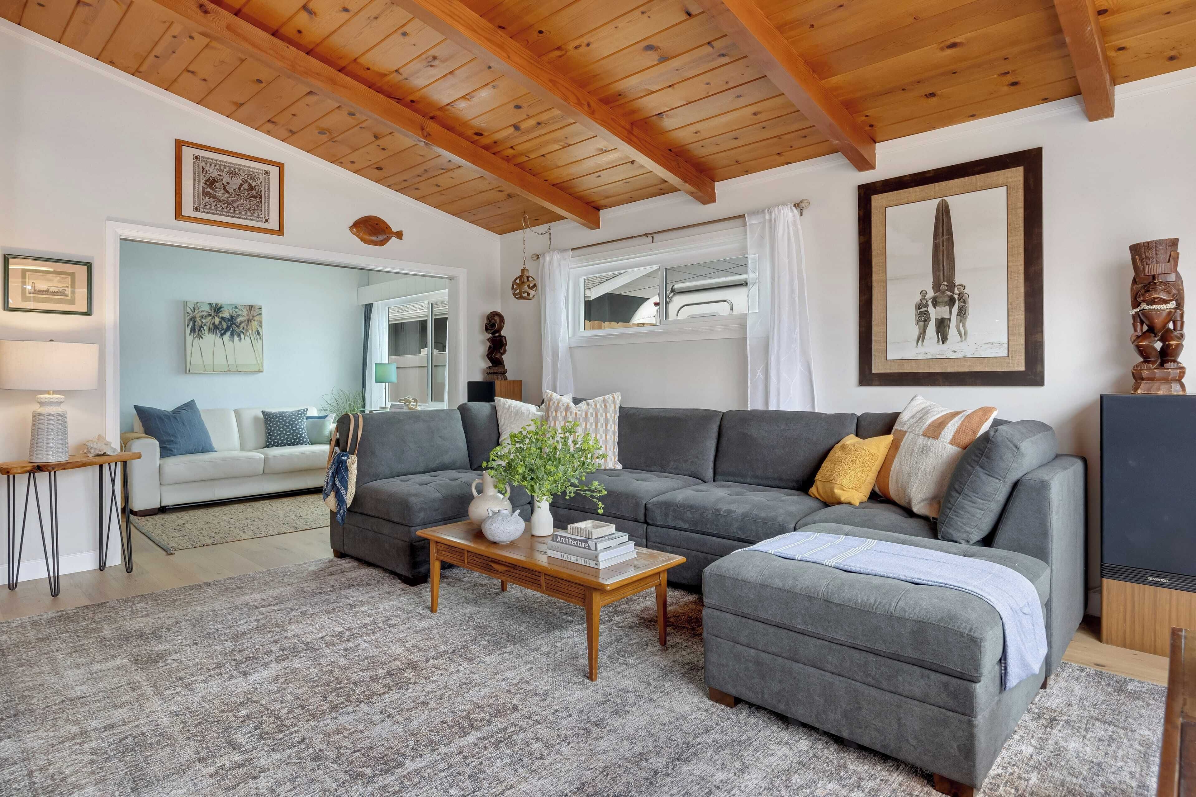 A living room with a gray sofa, a wooden coffee table, and a gray ottoman. There is a mirror, a lamp, and a framed picture on the wall.