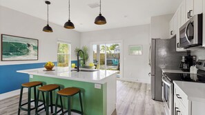 Uma cozinha moderna com ilha central, banquetas, geladeira e micro-ondas.